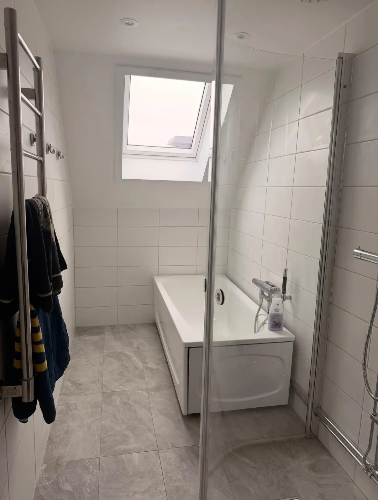 Vitt kaklat badrum med badkar under takfönster och ljusgrått klinkergolv