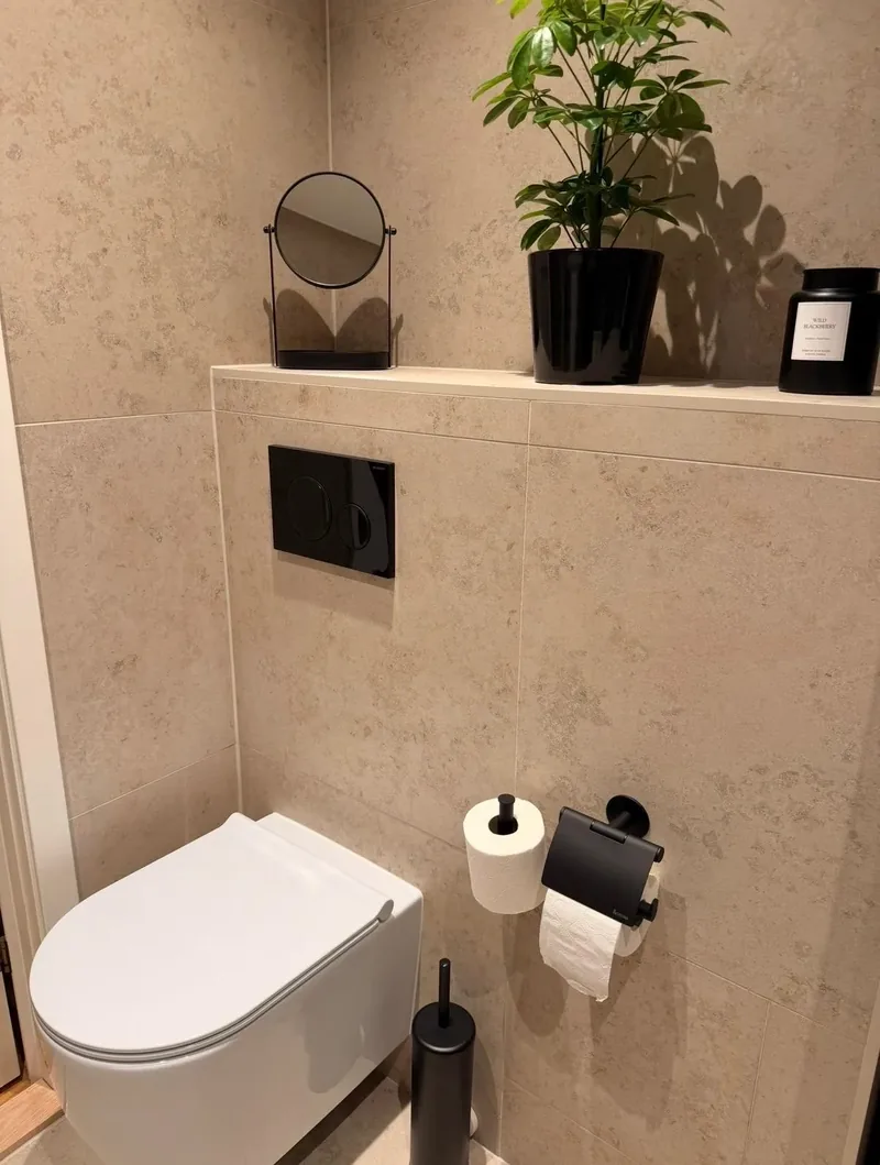 Vägghängd toalett mot beige kakel i kalkstensstil med svarta detaljer