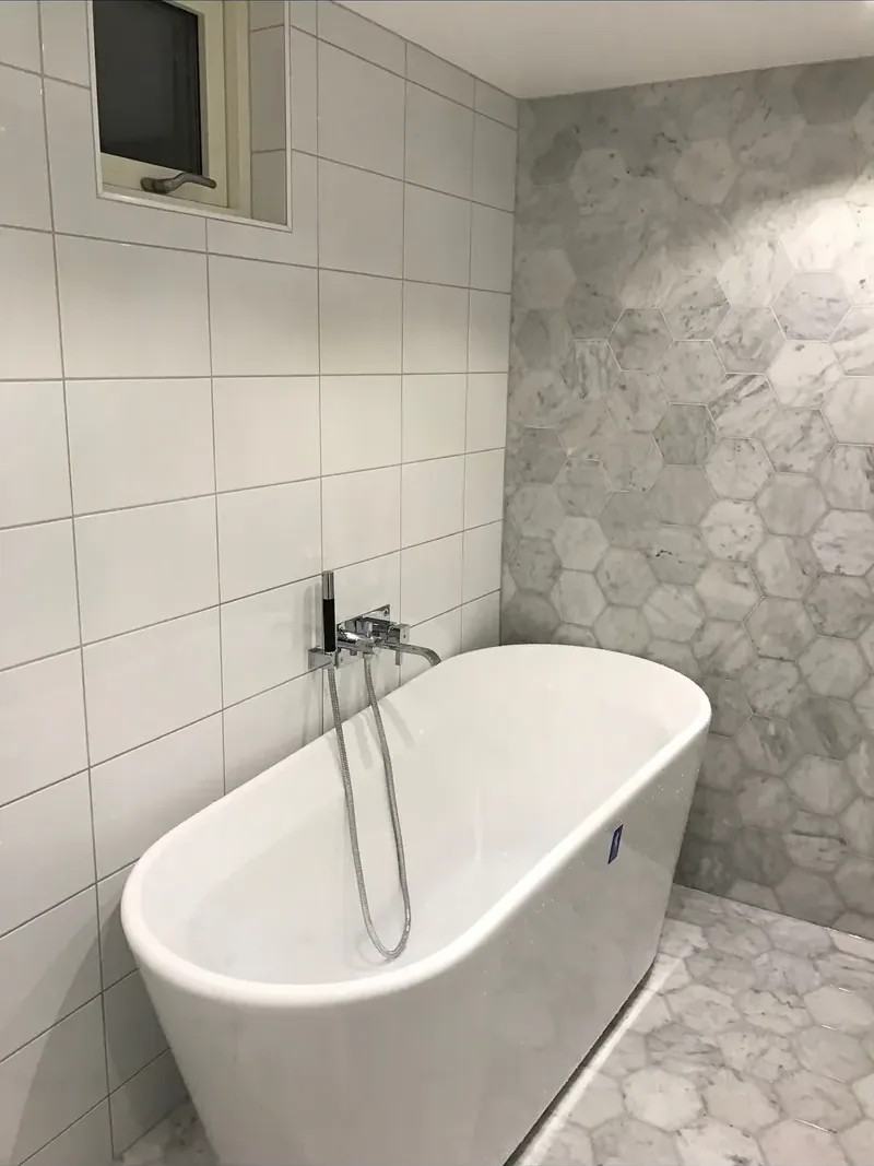Fristående badkar framför en vägg i grå marmor i sexkantsmönster