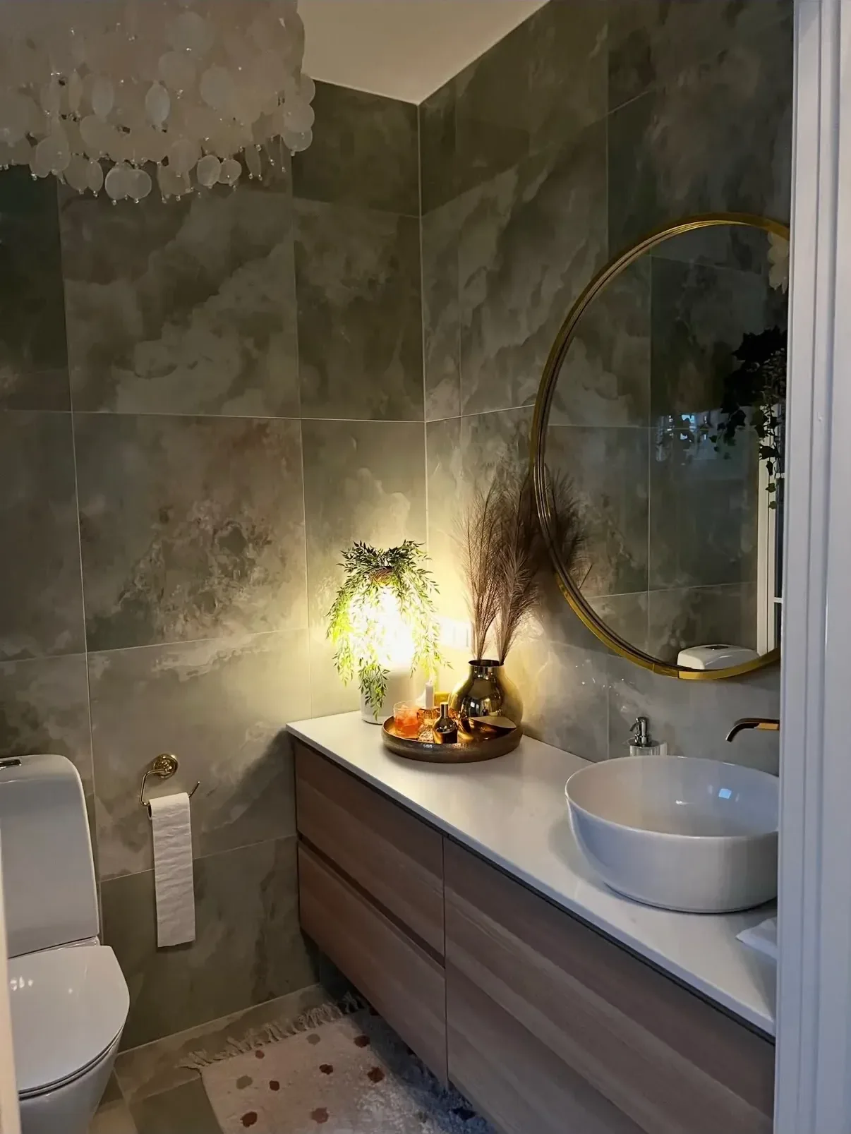 Badrum med stora gröngrå marmorplattor, rund mässingsspegel och kommod i valnöt med fristående handfat