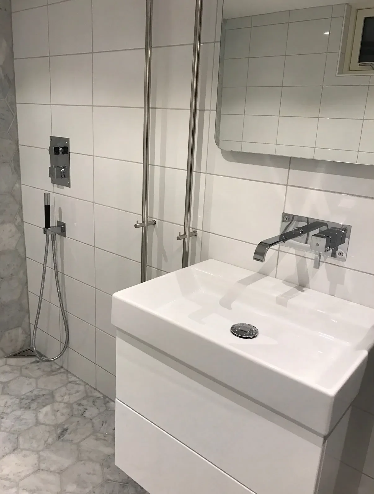 Vitt handfat med väggblandare och dusch i vitt kakel