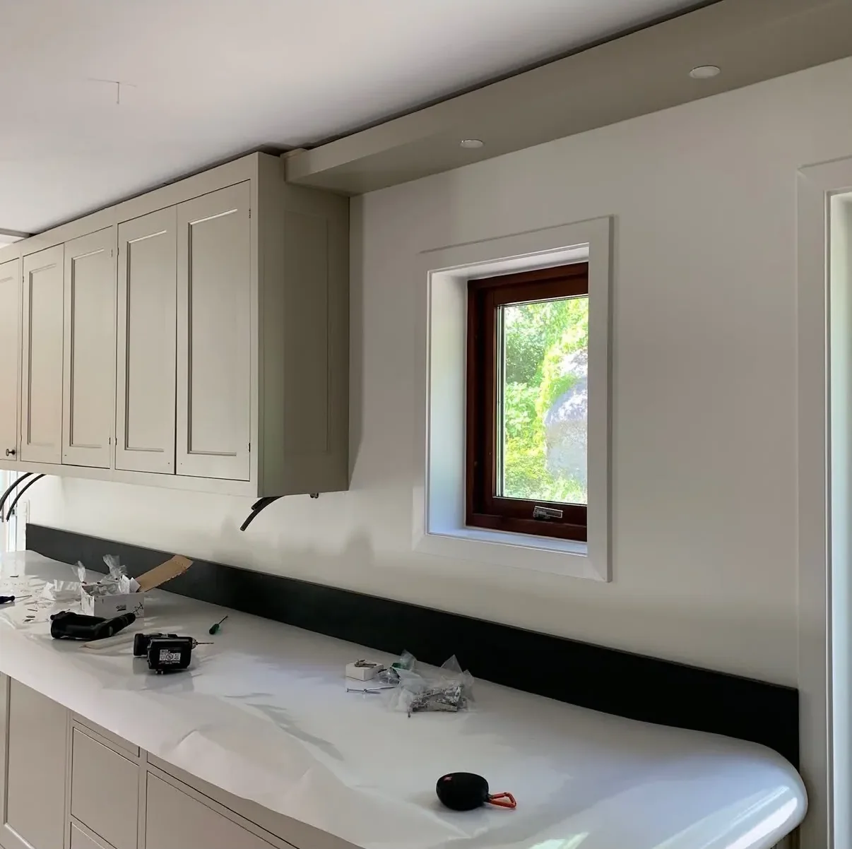 Kök under renovering med ljusa luckor, mörkt stänkskydd längs bänken och skyddspapper på bänkskivan